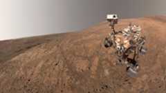 A rover sits on the reddish brownish surface of Mars