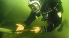 A diver holding a medieval spearhead under the murky waters of Lake Lednica in Poland.