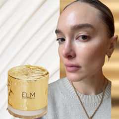 a white woman with glowing skin and her hair pulled back on a white and gold background with a gold jar next to her