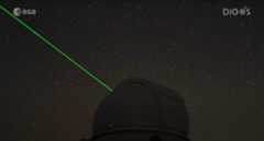 A bright green laser light shines from a darkened dome of an observatory into a starry night sky