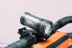 A large silver bike light mounted to the handlebars of a gravel bike