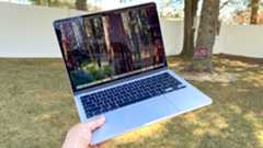 Person holding the MacBook Air 13-inch M4 outside above grass in a shaded garden