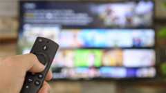 Hand holding a TV remote and using it to access a streaming service