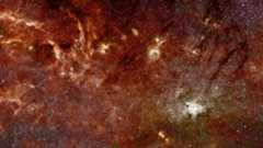 A panorama shows glowing reddish gas mixed with stars in deep space