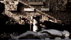 a plaster cast lies on its back in front of a wall of sculpture at Pompeii