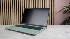 Three-quarter view of ASUS Chromebook CX15 open on desk with wooden panels, pink wall, and plant in background