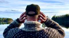 man with hands over ears in front of a lake