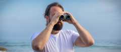 A male using the Canon 8x20 IS binoculars with the sea behind them.