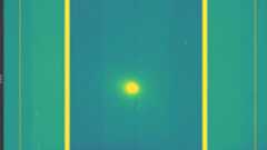 A screenshot of a yellow dot which is comet 3I/ATLAS in the middle of a green and purple background