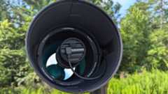 a black and white telescope in a field with trees behind it
