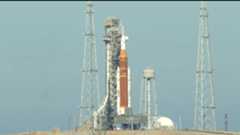 An orange and white rocket is held vertically by scaffolding on a launch pad.