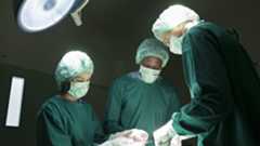 Low angle photo of three doctors in scrubs, gloves, and masks operating on a patient who is out of the frame.