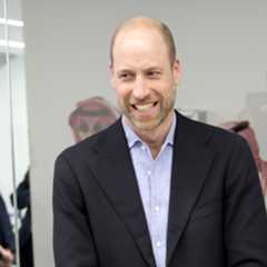 Prince William wearing a suit and laughing standing in a room with gamers