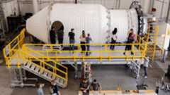 A series of people stand around a large space station in a giant warehouse