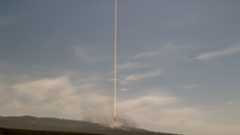 A daytime time lapse exposure of a rocket launch lifting off into partially cloudy sky.