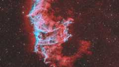A swirling red nebula is pictured against a distant starfield