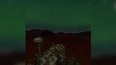 An illustration showing a rover sitting under a dark green sky full of northern lights flickering with stars.