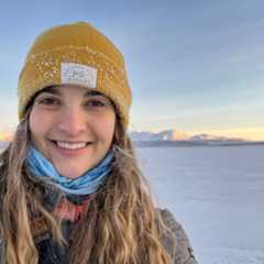 a woman wearing a yellow hat smiles under the blue light of the polar night.