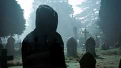 A double exposure horror edit. Of a hooded ghost like figure in a graveyard on an eerie foggy night