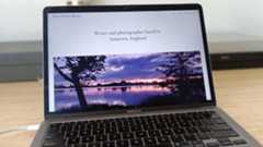 Laptop on desk showing website dominated by photo of sunset over a lake
