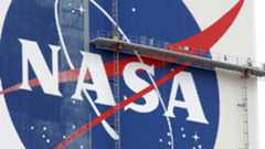 workers on scaffolding paint a nasa logo on a massive white building