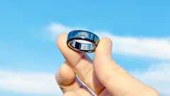 Close-up of the Oura Ring 4 shining in the sunlight in a user's hand with blue skies and clouds behind it