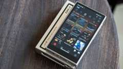 FiiO M21 music player lifestyle shot on a round wooden table with the screen active and showing icons for music tracks