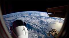 the blue waters and white clouds stretch to out to Earth's horizon, set against the blackness of space; in the foreground, a space capsule extends out from a space station