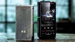 FiiO M27 front and back standing on a wooden surface in front of a very large but blurry windowed wall