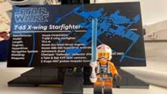 Lego Star Wars X-Wing Starfighter 75355-plaque front view with Rebel Pilot Luke minifigure standing in front holding blue lightsaber.