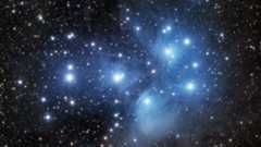 Pleiades star cluster appears as a group of bright blue stars surrounded by hazy clouds. 