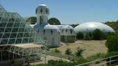 A series of glass domes stand next to other glass buildings on an arid compound with the hot desert sun beating down