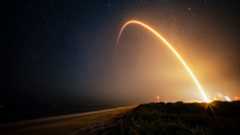 a time-lapse photo showing a streak from a rocket launch arcing over the beach at night.