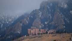 A series of adobe red buildings on a hillside with snowy mountains in the background