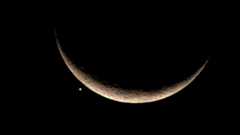 A picture of a thin crescent moon hanging against a black sky with the bright point of light representing Venus close to its lower left.