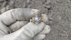 a person holds a gold ring covered in dirt with their fabric-gloved hand