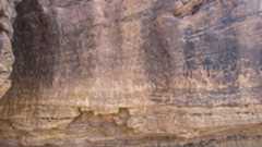 A sheer rock face of dark and light brown rock is covered with drawings and inscriptions