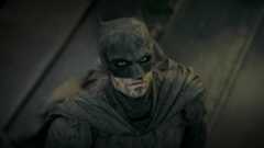 The Batman, as played by Robert Pattinson, looking up with hope, covered in ash and dust. 