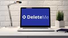 A laptop with the DeleteMe Logo on screen sits on a desk next to a lamp and a potted plant