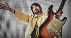 Simon Neil of Biffy Clyro wears a custard-colored jacket and green T-shirt and poses with a sunburst Fender Stratocaster