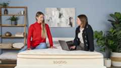 Two members of the Tom's Guide sleep team sit on the Saatva Classic mattress on a bed frame in our testing studio, discussing the comfort and support of the Saatva Classic, our number one mattress for most sleep styles