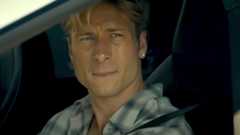 Glen Powell looking wistful staring out a car window wearing earrings in Chad Powers trailer. 