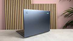 Rear three-quarter view of Acer Aspire 14 AI (2025), open on desk with wooden panel, plant, and pink wall in background