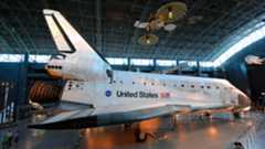 a white and black winged spacecraft is seen on display within a museum hangar