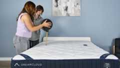 Two Tom's Guide testers setting up the motion isolation test. One is holding a 5kg slam ball above the mattress, while the other measures its height. An accelerometer is on the other side of the mattress