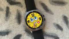 The Samsung Galaxy Watch 8 Classic resting on a blanket showing a custom Facer watch face of Spongebob Squarepants.
