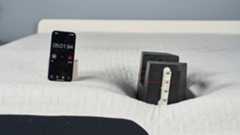 A closeup of the Nectar Premier Memory Foam Mattress on a bed frame in our sleep studio during the edge support test. A 25kg weight is balanced on the edge of the bed with a tape measure attached to the side. A red laser line is directed at the tape, indicating how far the weight has sank into the mattress. To the left, a phone displaying a stop watch is balanced. It indicates the test has been going on for 5 minutes 1 second.