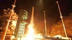 a white rocket lifts off into the night sky, its engine plume lighting the launch pad in white and orange hues.