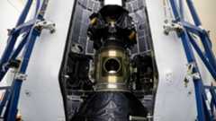 A large metal cylinder covered with black plastic is stood between blue scaffolding.