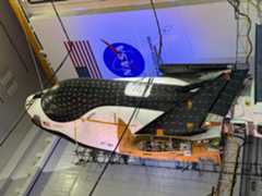 a black and white space plane stands on end in folded up in a hanger.